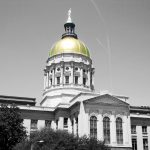 A photo of the Georgia State Capitol building rendered in black and white save its iconic gold-capped rotunda.