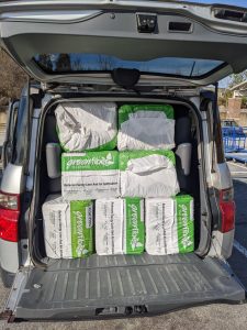 A small car packed full of cellulose insulation bales in a parking lot.